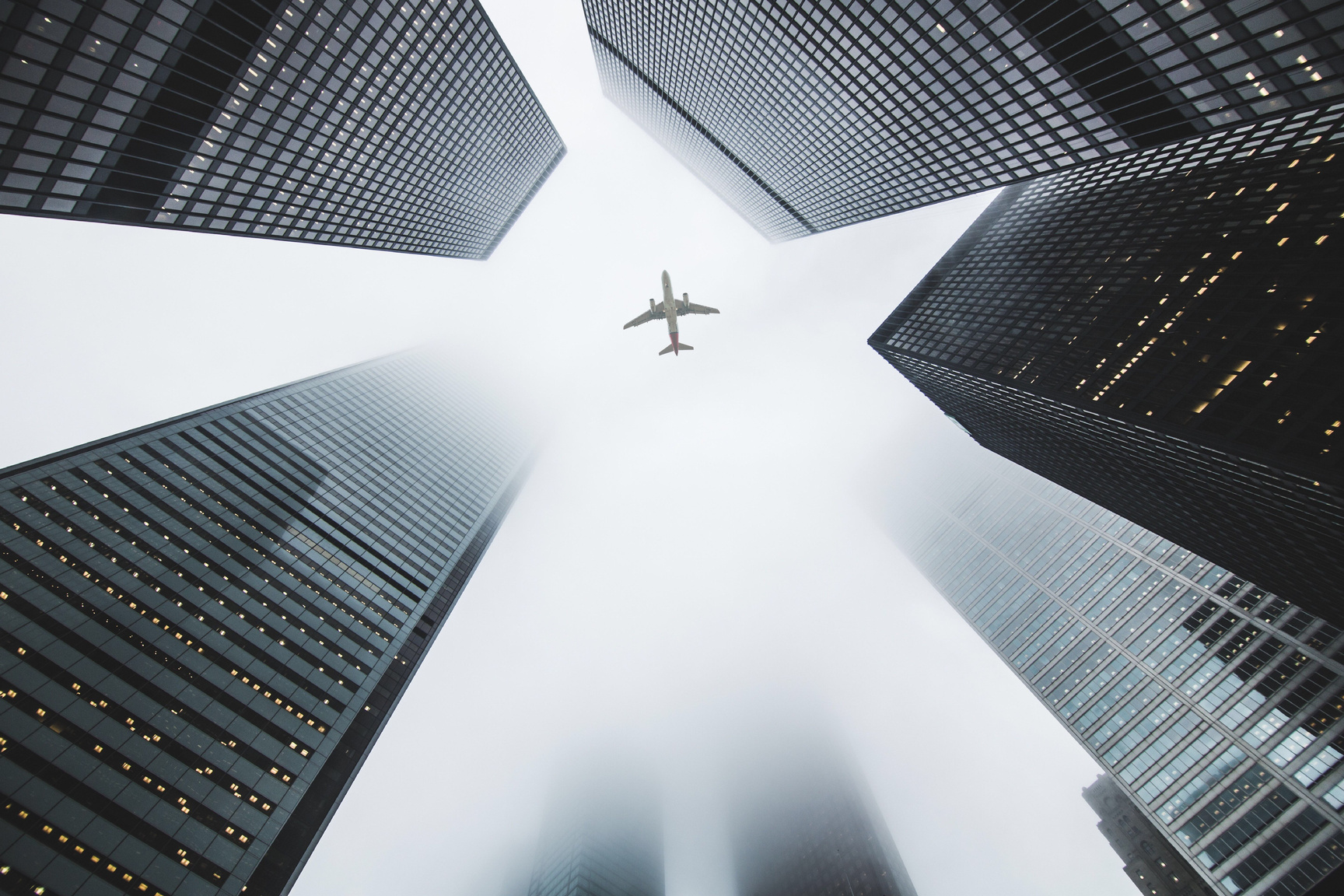 Low Angle Photo of Airplane Flying Over High-rise Buildings